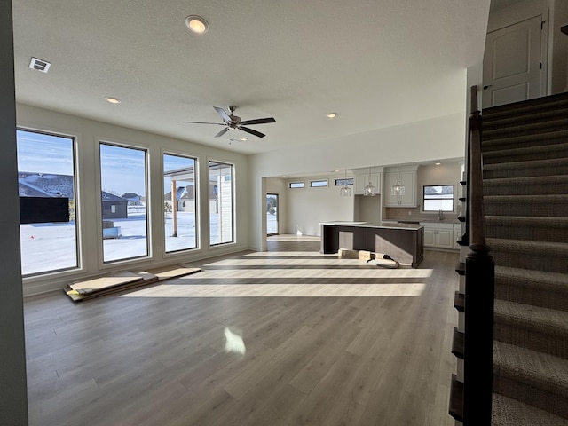 unfurnished living room featuring a textured ceiling, hardwood / wood-style flooring, ceiling fan, and sink