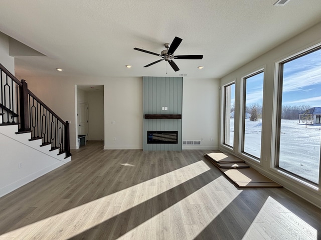 unfurnished living room with a large fireplace, ceiling fan, dark hardwood / wood-style flooring, and a textured ceiling