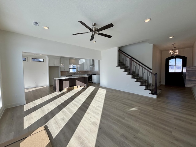 unfurnished living room featuring a textured ceiling, dark wood-type flooring, and ceiling fan with notable chandelier