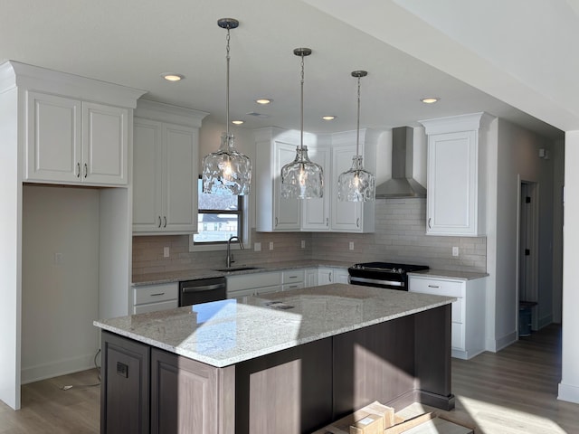 kitchen with sink, wall chimney range hood, a kitchen island, white cabinets, and black appliances