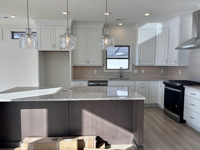 kitchen featuring white cabinets, wall chimney range hood, sink, decorative light fixtures, and stainless steel appliances