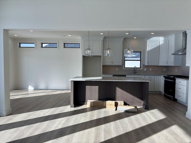 kitchen with sink, wall chimney range hood, black range with electric cooktop, decorative light fixtures, and a kitchen island