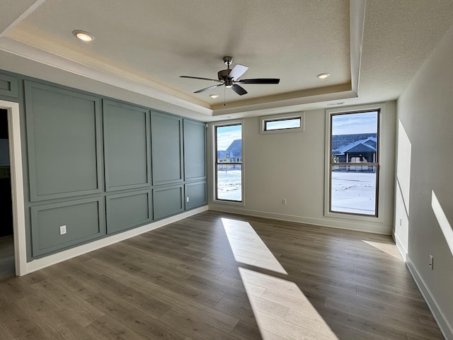 unfurnished room with a textured ceiling, ceiling fan, dark wood-type flooring, and a tray ceiling