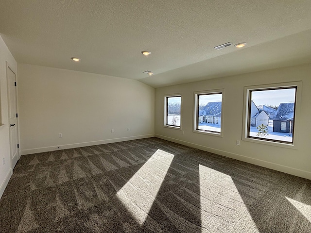 spare room featuring a textured ceiling, dark carpet, and vaulted ceiling