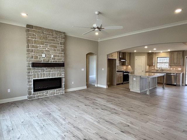 unfurnished living room featuring arched walkways, ceiling fan, a sink, light wood-style floors, and crown molding