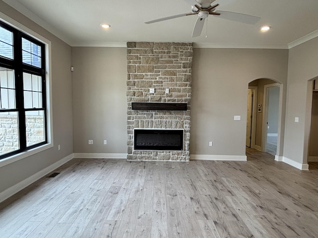 unfurnished living room featuring light wood-style floors, arched walkways, crown molding, and a fireplace