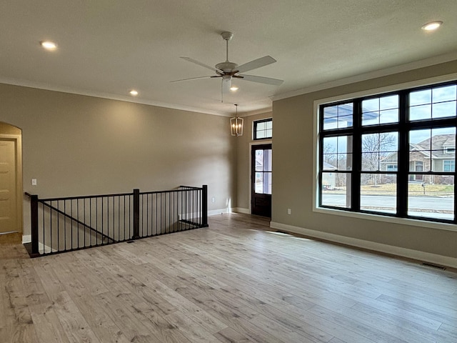 spare room with arched walkways, crown molding, visible vents, light wood-style floors, and baseboards