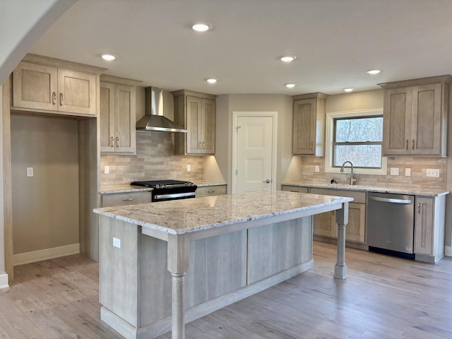 kitchen with a kitchen island, range with gas stovetop, wall chimney range hood, stainless steel dishwasher, and light wood-type flooring