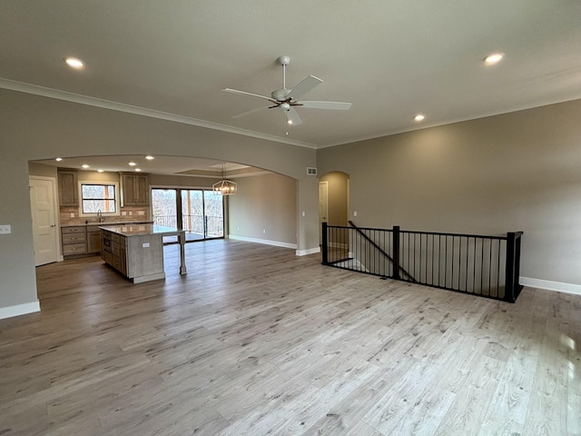 empty room with baseboards, arched walkways, light wood-style flooring, a sink, and ceiling fan with notable chandelier