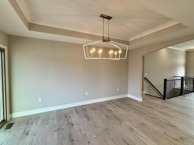 empty room with light wood-type flooring, baseboards, a tray ceiling, and a chandelier