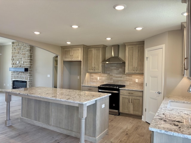 kitchen featuring a kitchen island, light stone counters, a kitchen breakfast bar, wall chimney range hood, and gas stove