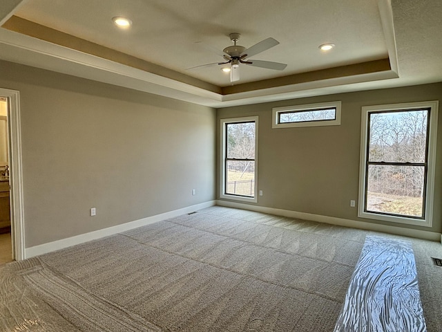 empty room featuring light carpet, recessed lighting, a raised ceiling, and baseboards