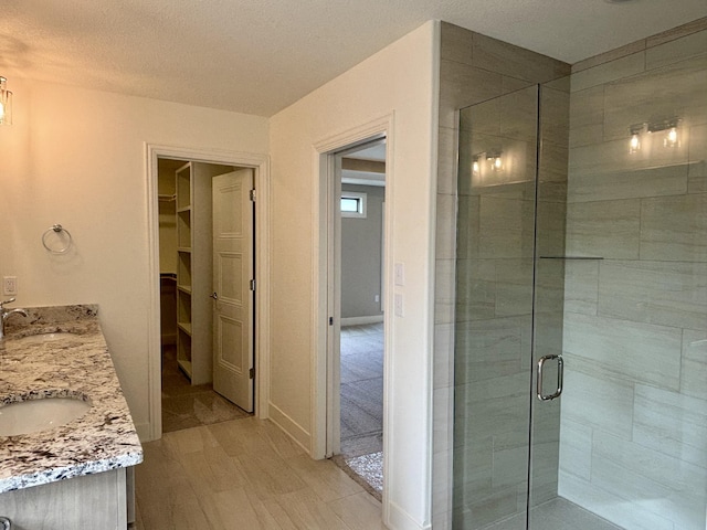 bathroom featuring double vanity, a stall shower, a sink, and a walk in closet