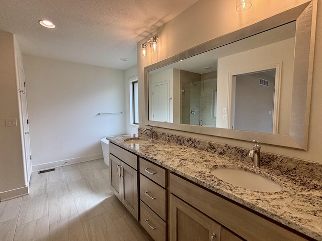 full bathroom featuring double vanity, a shower stall, a textured ceiling, and a sink