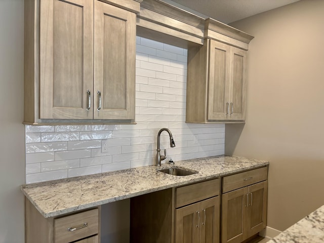 kitchen with baseboards, tasteful backsplash, a sink, and light stone countertops