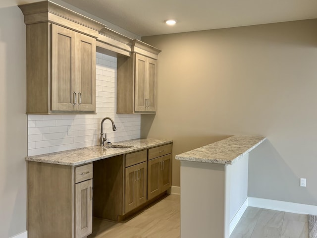 kitchen featuring light stone counters, tasteful backsplash, recessed lighting, a sink, and baseboards