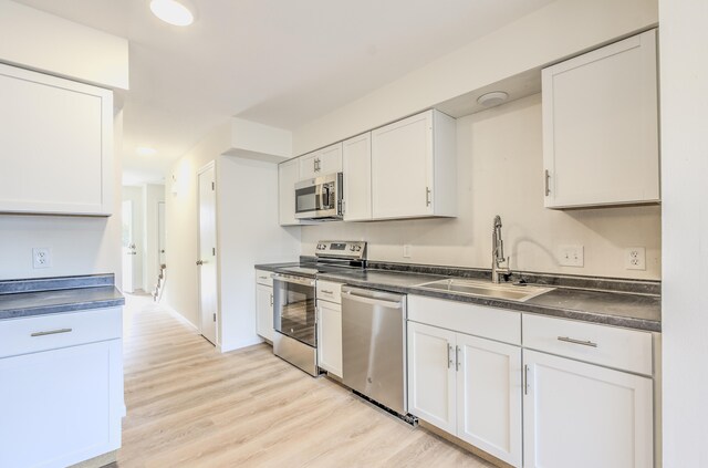 kitchen with stainless steel appliances, white cabinets, sink, and light wood-type flooring