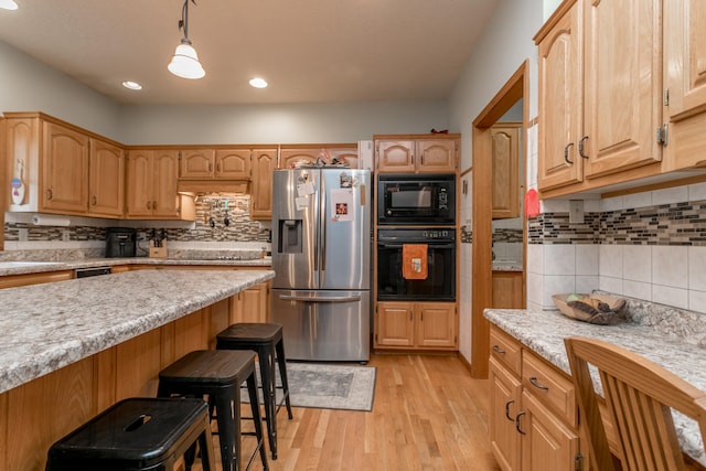 kitchen featuring black appliances, backsplash, decorative light fixtures, light hardwood / wood-style floors, and a breakfast bar