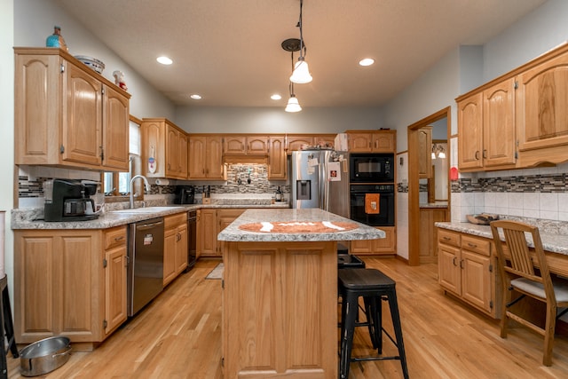 kitchen featuring sink, black appliances, a kitchen bar, light hardwood / wood-style flooring, and a center island