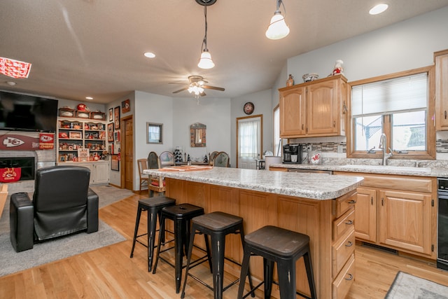 kitchen with sink, ceiling fan, a kitchen island, a breakfast bar, and light hardwood / wood-style flooring