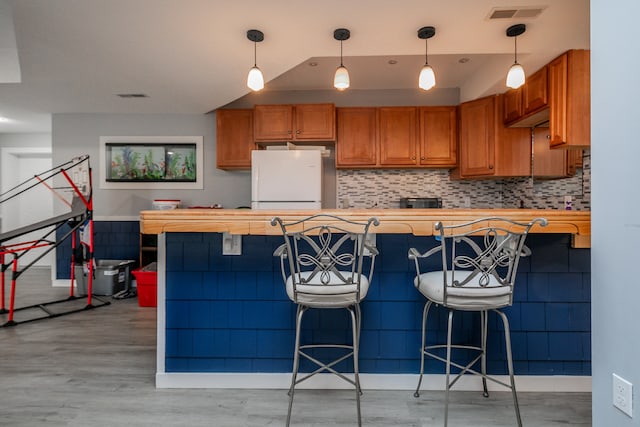 kitchen with pendant lighting, a breakfast bar area, white refrigerator, and light hardwood / wood-style flooring