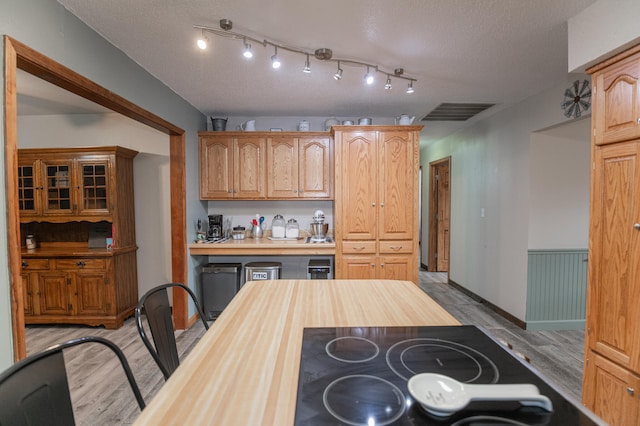 kitchen featuring butcher block countertops, black electric stovetop, a textured ceiling, and light hardwood / wood-style flooring