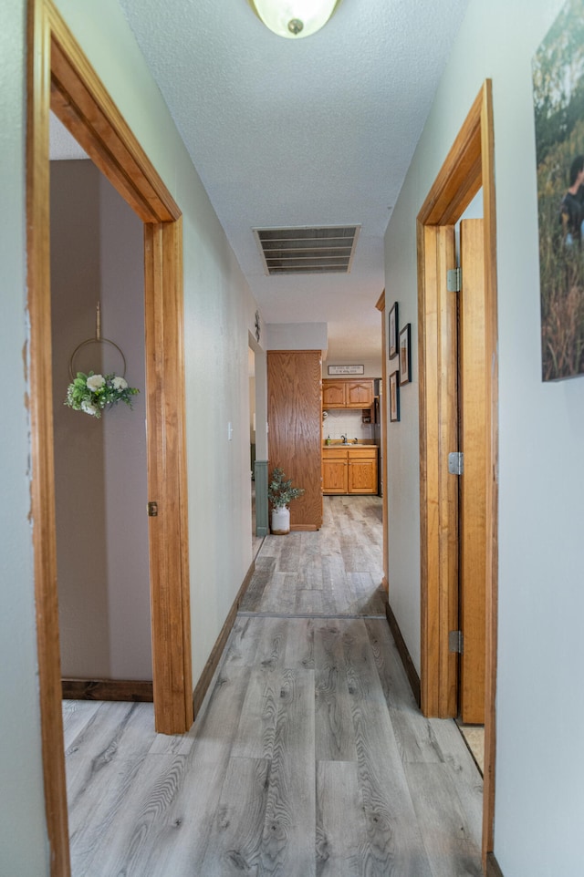 hall with a textured ceiling and light wood-type flooring