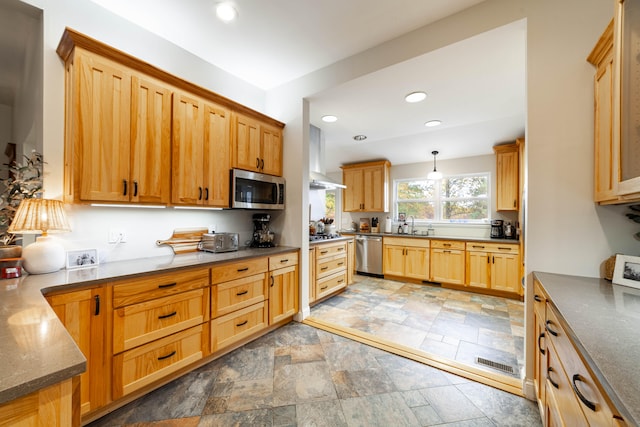 kitchen featuring wall chimney range hood, sink, pendant lighting, and appliances with stainless steel finishes