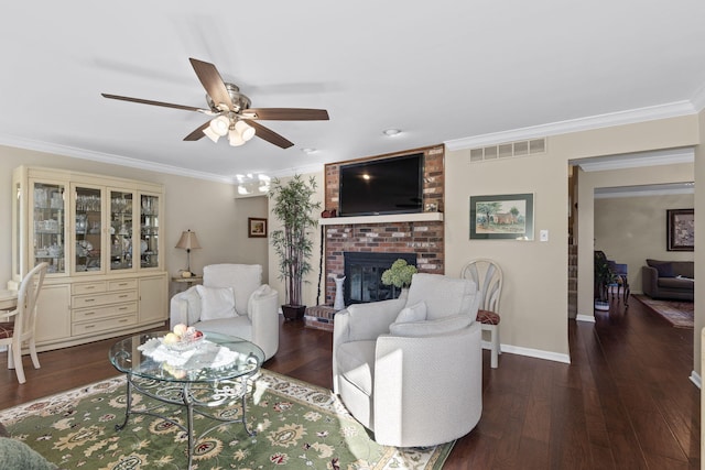 living room with dark wood-type flooring, ceiling fan, crown molding, and a brick fireplace