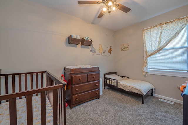 carpeted bedroom featuring a nursery area and ceiling fan