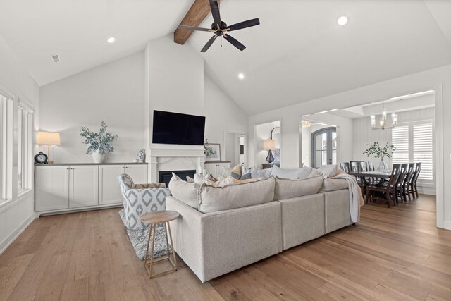 living room with high vaulted ceiling, beam ceiling, ceiling fan with notable chandelier, and light hardwood / wood-style flooring