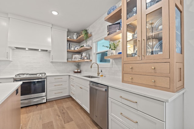 kitchen with premium range hood, appliances with stainless steel finishes, sink, white cabinets, and light hardwood / wood-style flooring