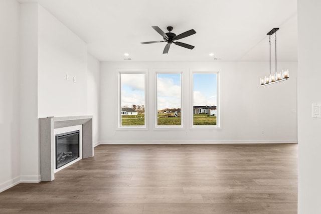 unfurnished living room featuring ceiling fan with notable chandelier and wood-type flooring