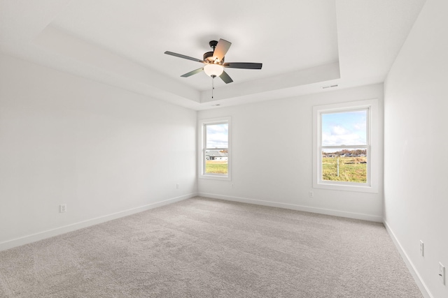 carpeted empty room with a healthy amount of sunlight, a raised ceiling, and ceiling fan