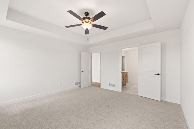 unfurnished bedroom with a tray ceiling, light carpet, ceiling fan, and ensuite bathroom