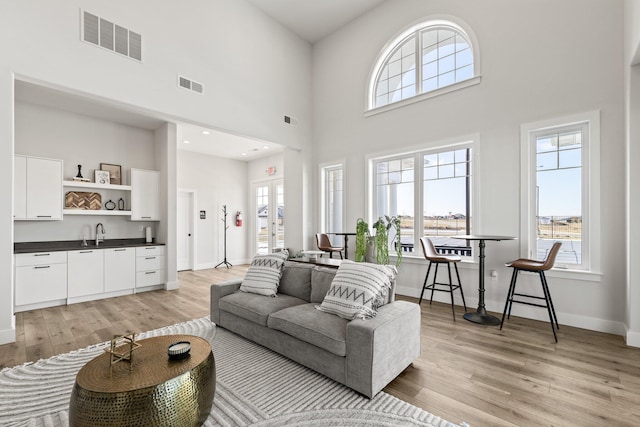 living room featuring light wood-type flooring, sink, and a high ceiling