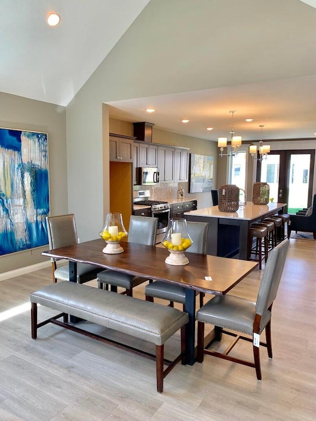 dining space with an inviting chandelier, vaulted ceiling, and light hardwood / wood-style floors