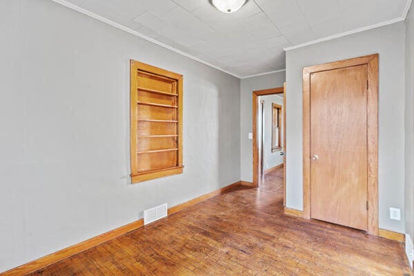 empty room with hardwood / wood-style floors and ornamental molding