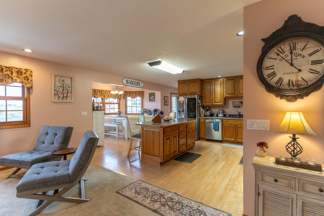 kitchen with stainless steel appliances, a kitchen bar, an inviting chandelier, light hardwood / wood-style floors, and a center island