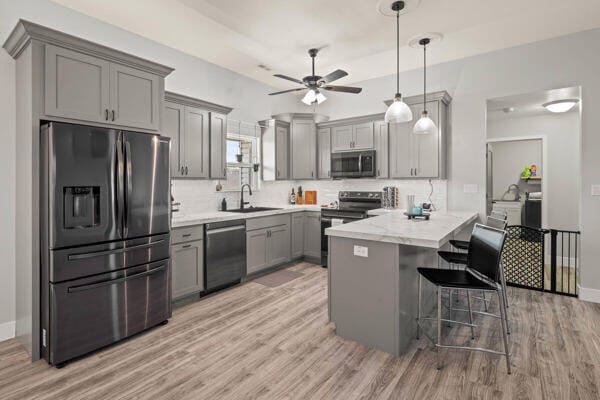 kitchen featuring a breakfast bar, light hardwood / wood-style flooring, decorative light fixtures, kitchen peninsula, and stainless steel appliances