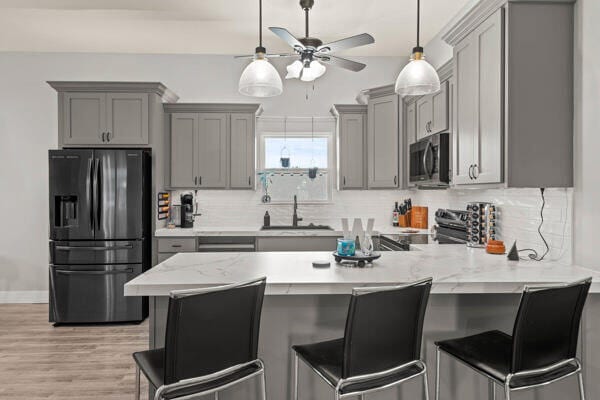 kitchen featuring a kitchen breakfast bar, tasteful backsplash, kitchen peninsula, appliances with stainless steel finishes, and light wood-type flooring