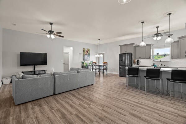 living room featuring ceiling fan with notable chandelier and light hardwood / wood-style flooring