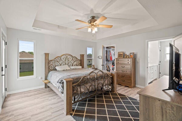 bedroom with hardwood / wood-style floors, ceiling fan, a raised ceiling, and a spacious closet