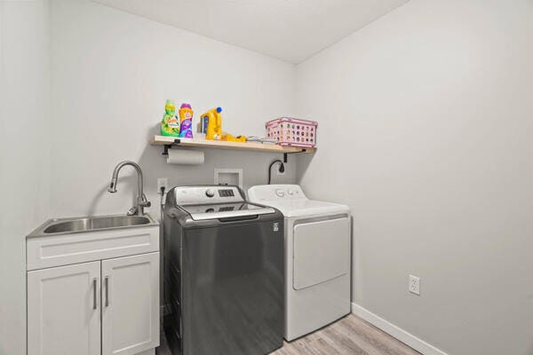 clothes washing area with washer and clothes dryer, cabinets, light wood-type flooring, and sink