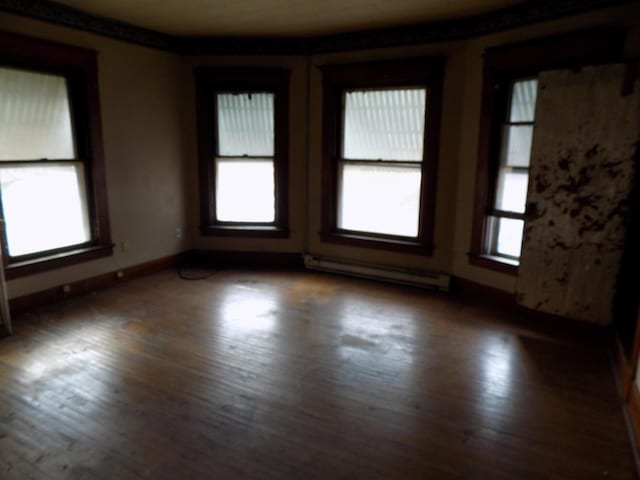 unfurnished room featuring baseboard heating and dark wood-type flooring