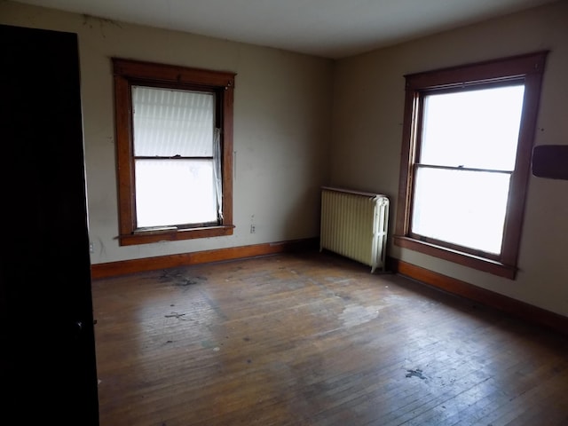 unfurnished room featuring wood-type flooring, radiator heating unit, and a wealth of natural light