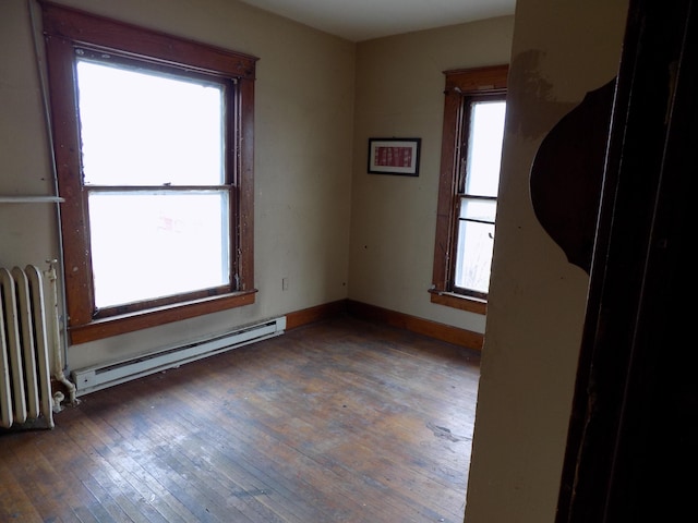 unfurnished room featuring plenty of natural light, dark hardwood / wood-style floors, baseboard heating, and radiator