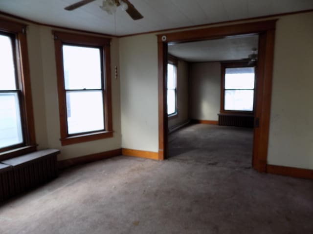 carpeted spare room featuring ceiling fan, a healthy amount of sunlight, and radiator heating unit