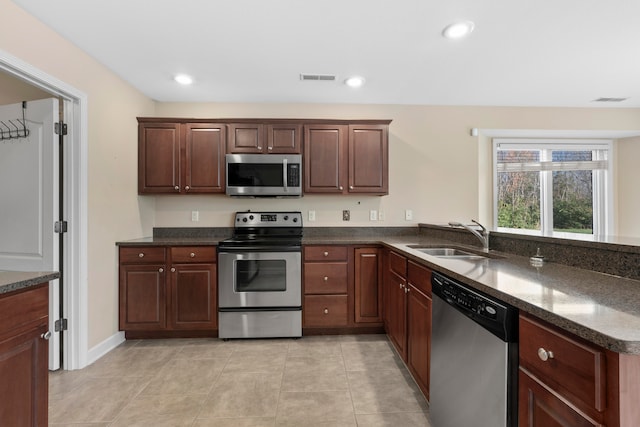 kitchen featuring sink, dark stone countertops, light tile patterned floors, appliances with stainless steel finishes, and kitchen peninsula