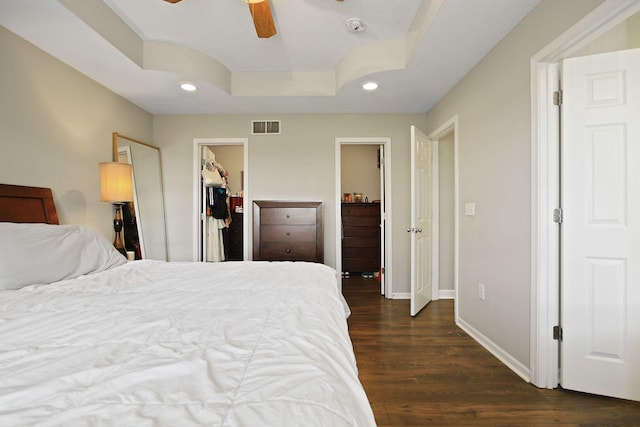 bedroom featuring dark wood-type flooring, a walk in closet, a raised ceiling, a closet, and ceiling fan